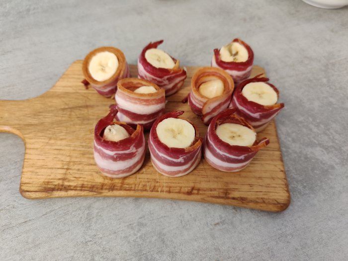 Skivor av banan lindade med bacon på ett skärbräde redo att grillas.