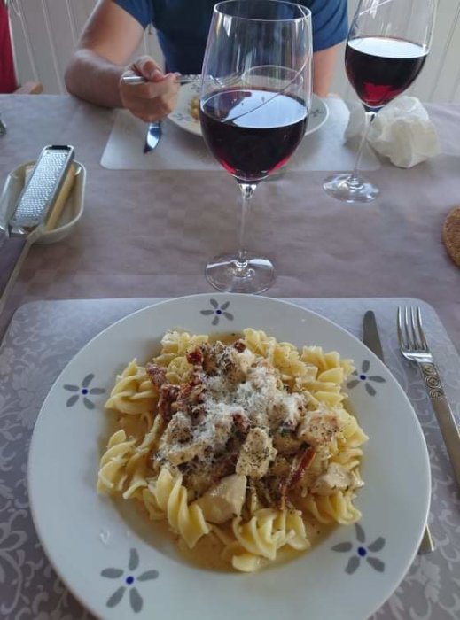 Tallrik med pasta och kyckling toppad med basilika och soltorkade tomater, glas rödvin, firar bröllopsdag.