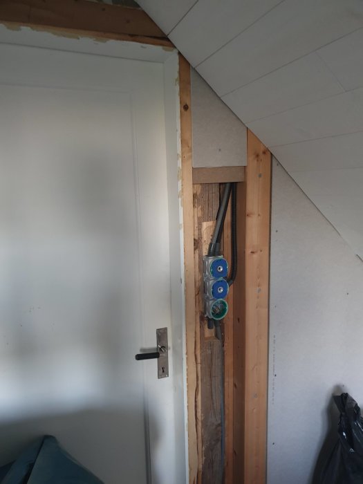 Renoveringsprojekt som visar en öppen vägg med synliga rör och elledningar nära en vit dörr.