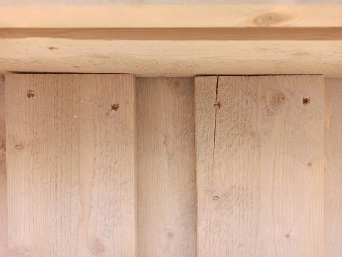 Träpanel med sprickor under en horisontell bjälke, indikerar skador i byggprojekt.