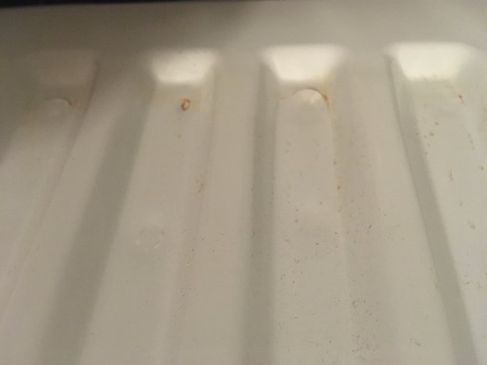 Närbild på en vit Purmo t22 radiator med färgsläpp och svetspunkter längs överdelen.