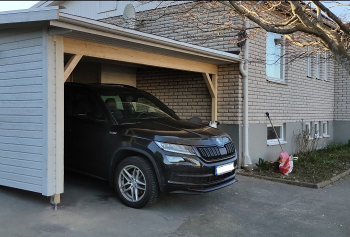 Bil parkerad under carport med ljus tegelfasad och grå husgrund i behov av målning.