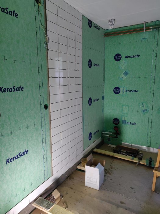 Delvis kaklade väggar i ett pågående renoveringsprojekt med verktyg och byggmaterial synliga.