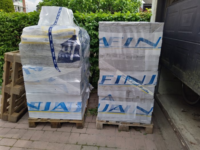 Två pallar med inplastade byggmaterial bredvid en garageuppfart.