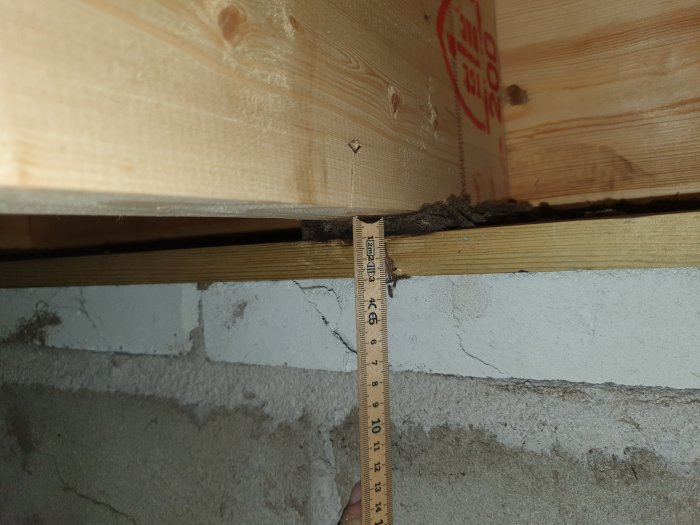 Mätning av avståndet mellan en nylagd impregnerad syll och en gammal asfaboard i ett hus under renovering.