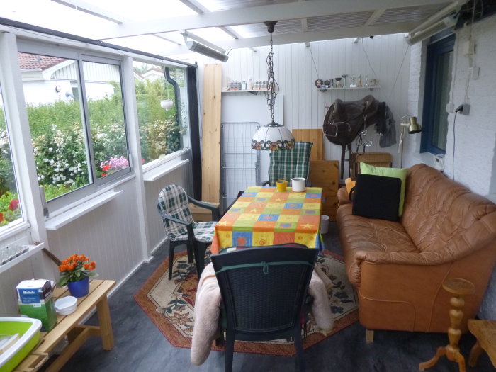 Inglasat uterum med soffa, köksbord, stolar och odlingstillbehör, utsikt till trädgård.