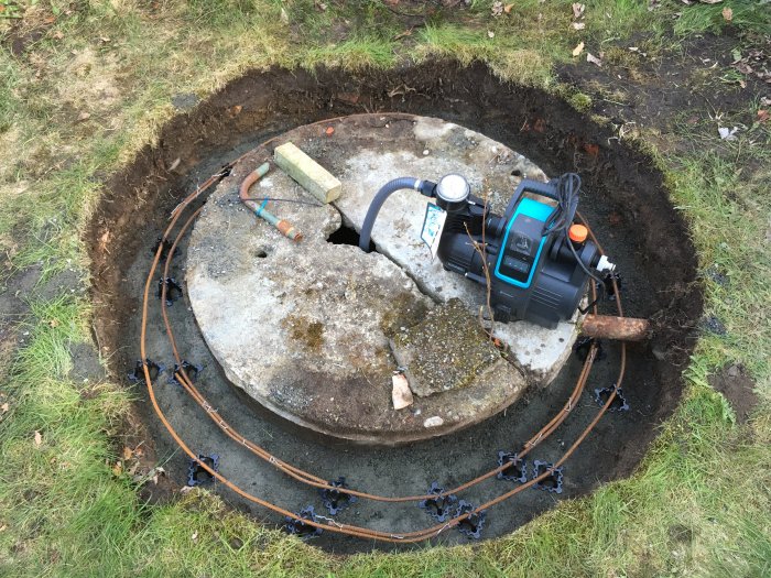 Brunnslock med pågående murarbete och en vattenpump placerad ovanpå i ett grävt hål.