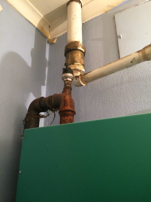 VVS-installation med vit och rostig vattenledning ovanför en grön vägg.