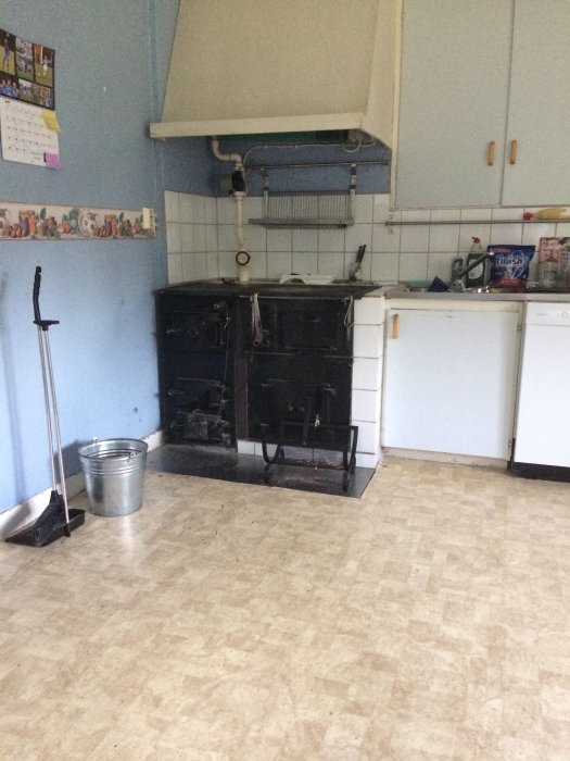 Gammal köksinredning med vedspis, skåp och diskbänk i en bostad under renovering.