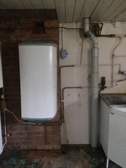 Värmesystem i källare med varmvattenberedare, rörsystem och tvättställ.