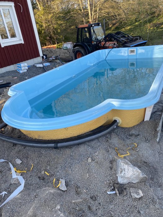 Halvinstallerad pool med isolering synlig och grävmaskin i bakgrunden under pågående byggarbete.