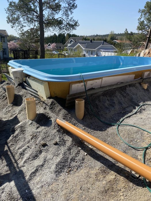 Pool under konstruktion med omgivande grus och gjutrör förberedda för altanstomme.