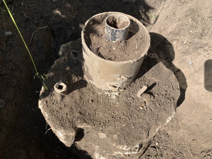 Ett grävt hål som avslöjar en stor cementklump med krokar och rör i marken.