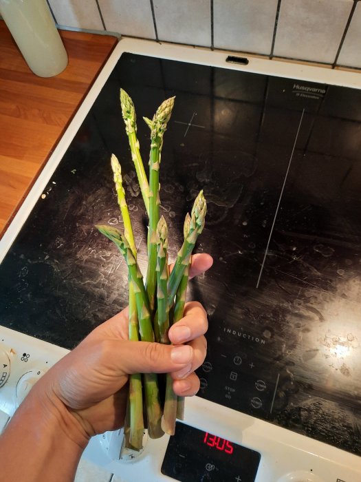 Hand som håller en bunt sparris framför en induktionshäll.