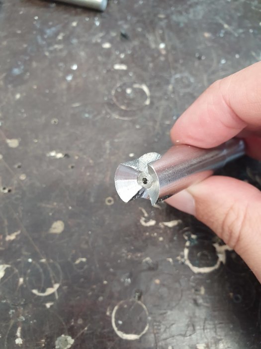Hand håller ett metallborr med slipade kanter mot en slitstark arbetsbänk.