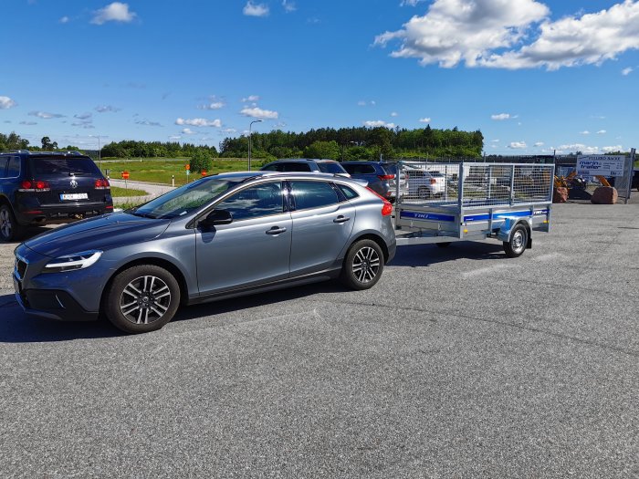 Bil kopplad till en ny rikiTIKItrailer på en parkeringsplats under solig himmel.