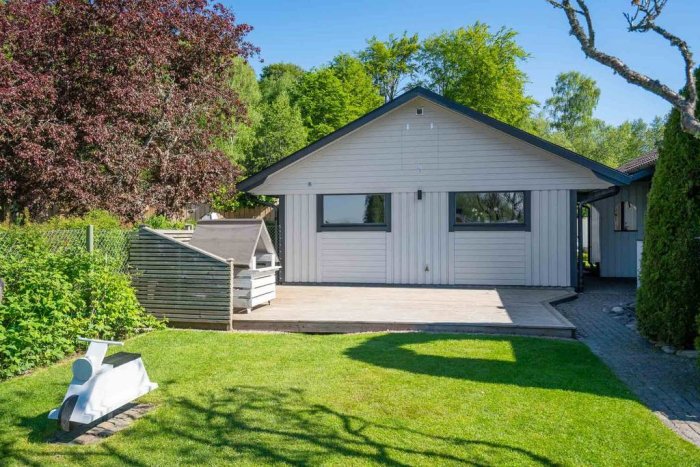 Ett nyligen sålt enfamiljshus med vit panel och garage i somrigt grönskande område.