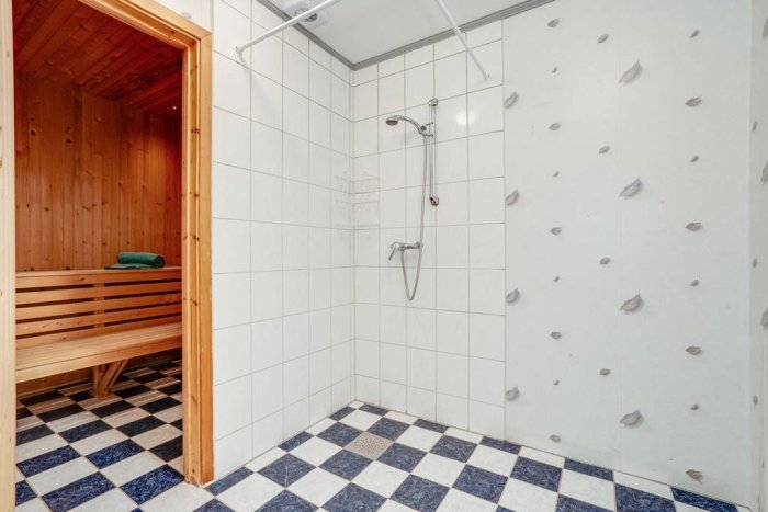 Badrum med öppen dörr till bastu och intilliggande duschkabin med kakelväggar.