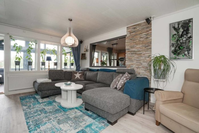 Vardagsrum med grå soffa, blått överkast, vitt runt soffbord, och stenvägg, sett inifrån.