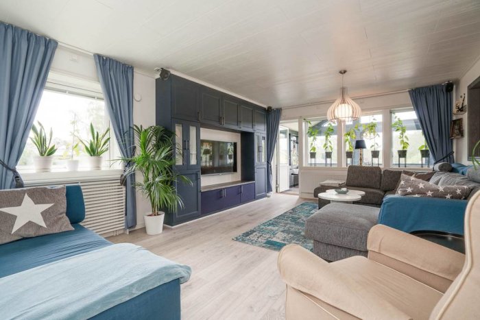 Elegant inrett vardagsrum med blåa accenter, möbler och växter framför fönstret.