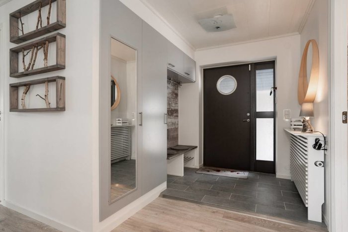 Vy inifrån ett hem med entrédörren, badrumsdörr, spegel och dekorativa element.