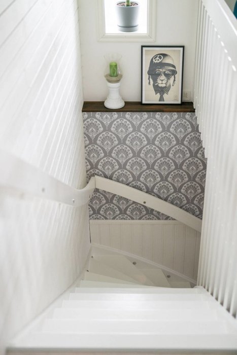 Trappa nedåt med vit räcke, mönstrad tapet och inramad illustration på väggen.