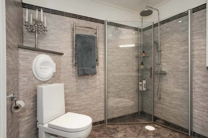 Modernt badrum med duschhörna, toalett och ljuskrona på väggen.