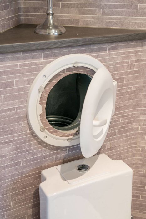 Öppen inspektionslucka ovanför en toalettstol mot en kaklad vägg.