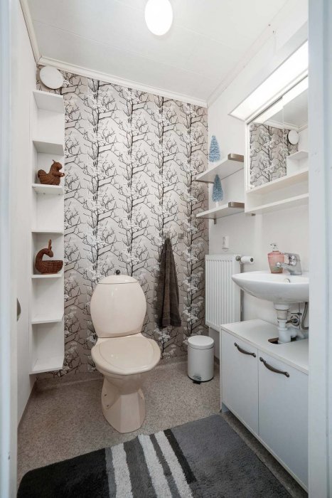 Ett modernt badrum med växtmönstrad tapet, vit inredning och grått golv.