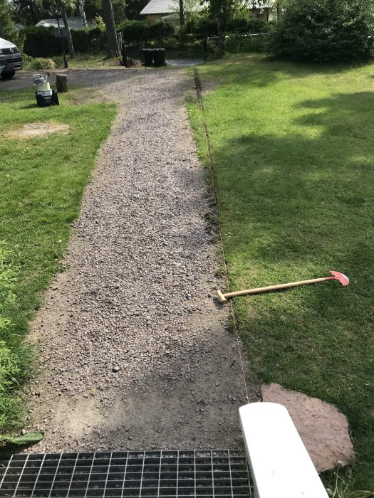 Grusgång med nyskuren kant längs gräsmattan och en röd kantskärare till höger, med synliga grindstolpar i bakgrunden.