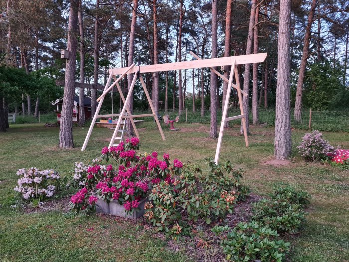 Nytt träställ till gungställning under konstruktion i en trädgård med blommande buskar.