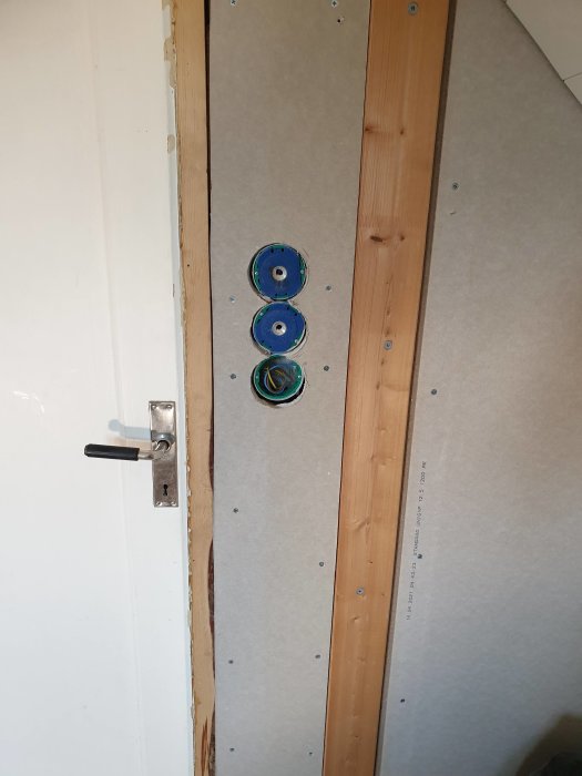 En nyinstallerad trästolpe i linje med en vit vägg, med elektriska dosor på gipsskiva redo för spackling.