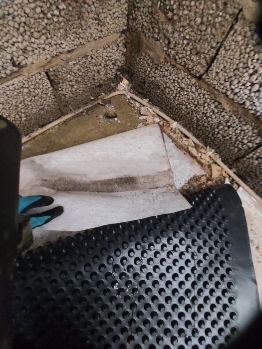 Upprivet golv med synlig vattenskada och blött material på betong samt vattenfylld platonmatta.