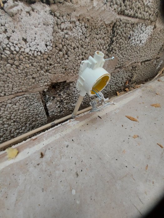 Uppbrutet golv med synlig platonmatta, frigolit och vattenläckage vid betongvägg och elinstallation.