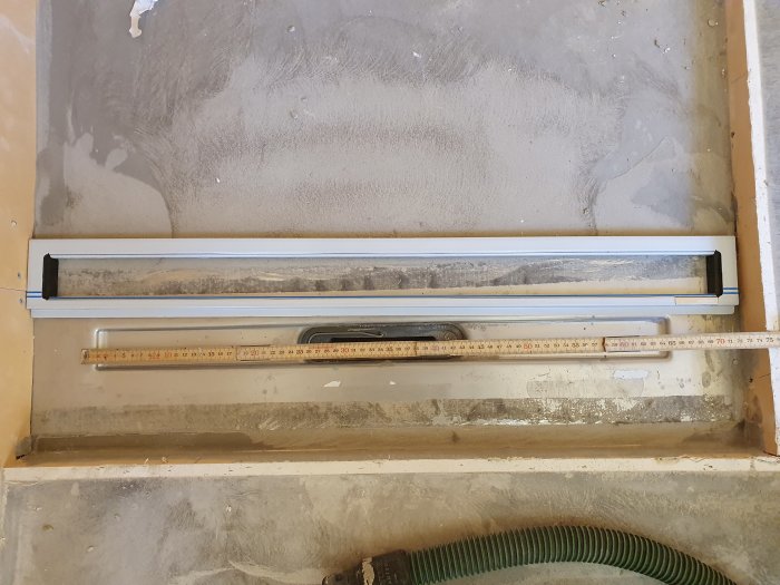 Grått betonggolv med infälld dörrtröskel och mätsticka framför för storleksreferens.