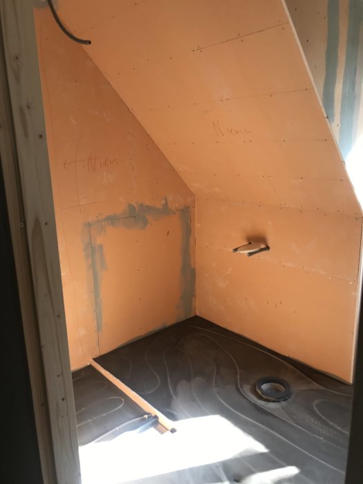 Pågående badrumsrenovering med oavslutad väggisolering och synliga vattenrör på golvet.