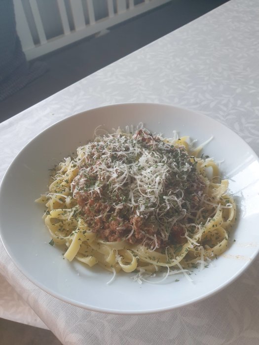 En tallrik med tagliatelle toppad med viltragu och riven ost, serverad på ett vitt bord.