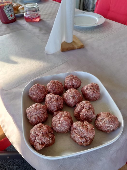 Råa köttbollar av kryddad köttfärs på ett fat redo för matlagning, med ketchup i bakgrunden.