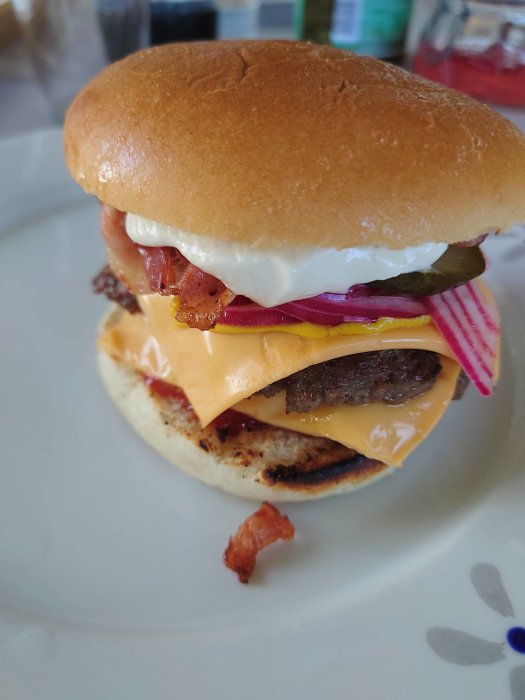Hamburgare med köttfärsbiffar, ost, bacon, rödlök och pickles på en tallrik.