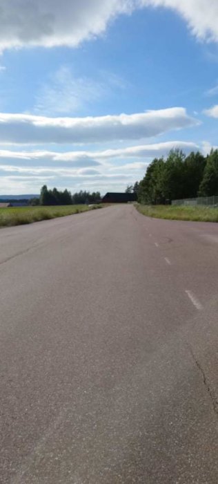 Asfalterad landsväg med vita linjer som sträcker sig mot horisonten och en blå himmel med moln.