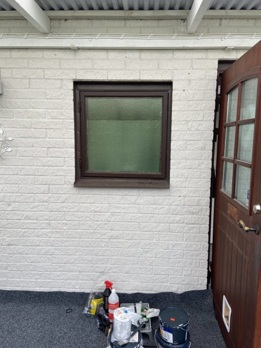 Altan före renovering med ett fönster, vitmålad vägg och renoveringsmaterial på golvet.