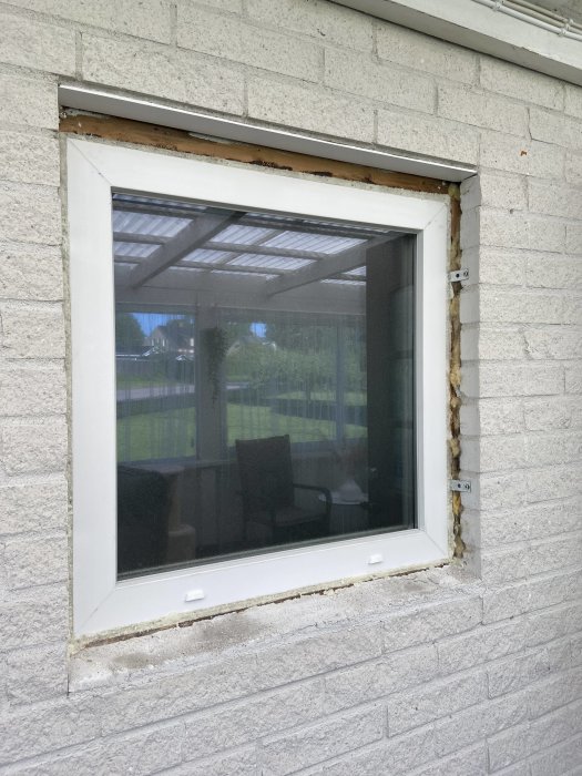 Nytt bleck runt toalettfönster på vit tegelvägg, isolering synlig utanför fönsterkarmen.