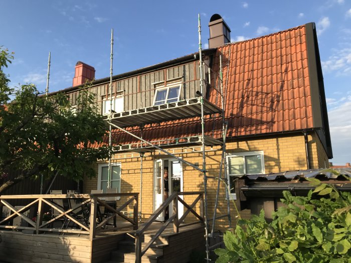 Renoverad gavel med nytt virke, vindskivor och plåt på ett gult hus med ställningar.