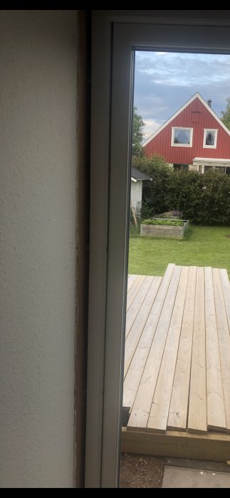 Gap mellan en dörr och karmen på vänster sida uppåt, utsikt till trädgård och rött hus.