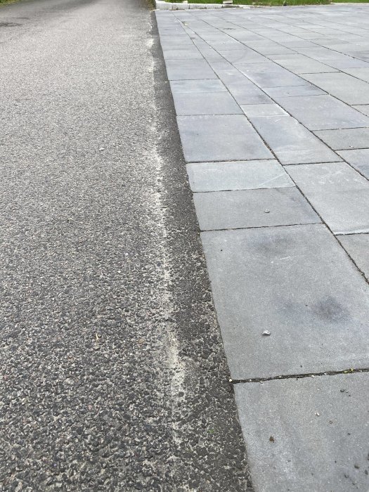 Välgående grå betongplattor bredvid asfalterad väg, linjen mellan dem är rak och klar.