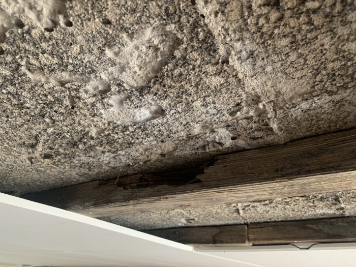 Ojämnt betongtak med vittrade träreglar synliga underifrån, problem med fuktträngning.