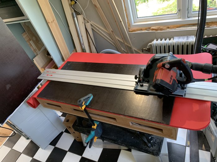 Cirkelsåg på skena används på en röd yogamatta för att såga i en formplywoodskiva på ett arbetsbord.