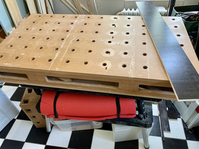 Hantverksrum med en röd yogamatta under en arbetsbänk med spånskiveplatta och formplaywood.