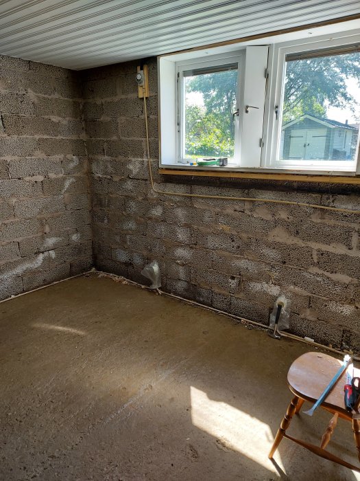 Renoverat källarrum med uppgrävt betonggolv, exponerade murade väggar och ett fönster som släpper in sol.