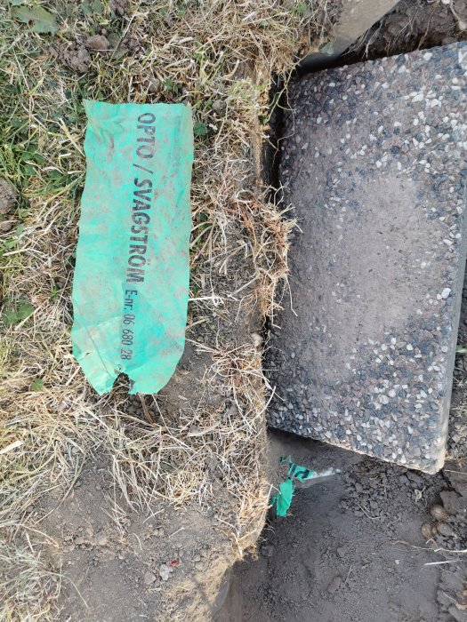 Grävd rabatt med varningsband för optokabel ca 15-20 cm under ytan, nära asfaltkant.